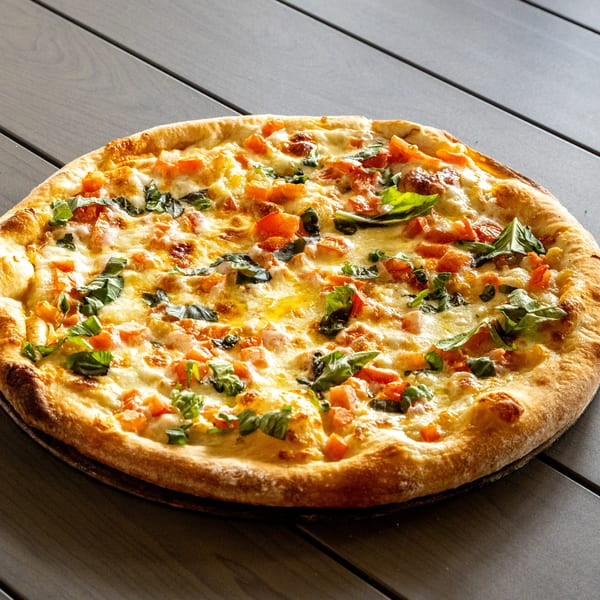 Annie's Pizza with melted cheese, diced tomatoes, and fresh basil on a dark wooden table.