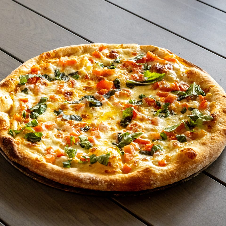 Annie's Pizza with melted cheese, diced tomatoes, and fresh basil on a dark wooden table.