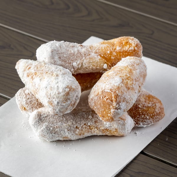 A pile of golden-brown, powdered sugar-dusted zeppole on white parchment paper, against a dark wooden table.