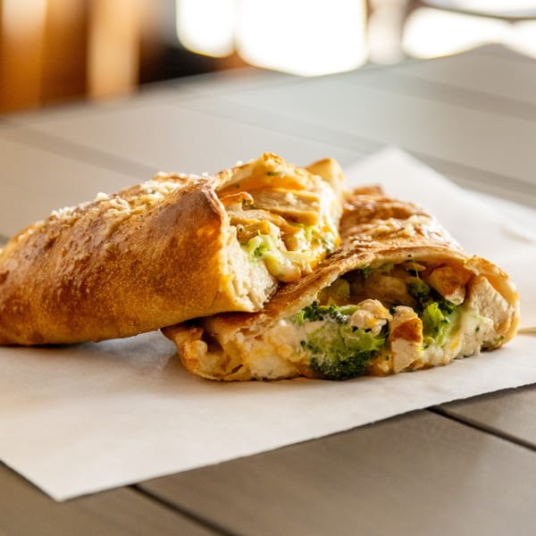 Two Annie's Pizza Subs & Wings calzones filled with chicken, broccoli, and cheese on parchment paper.