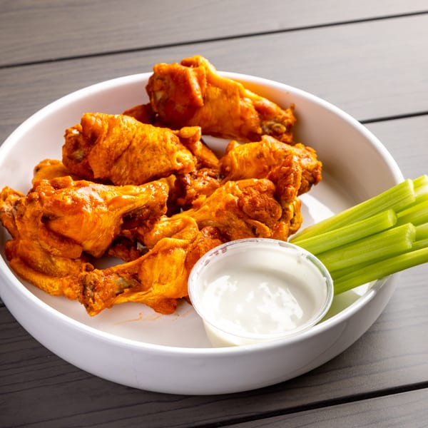 A white bowl of Annie's Pizza Subs & Wings' buffalo wings, celery sticks, and ranch dressing.