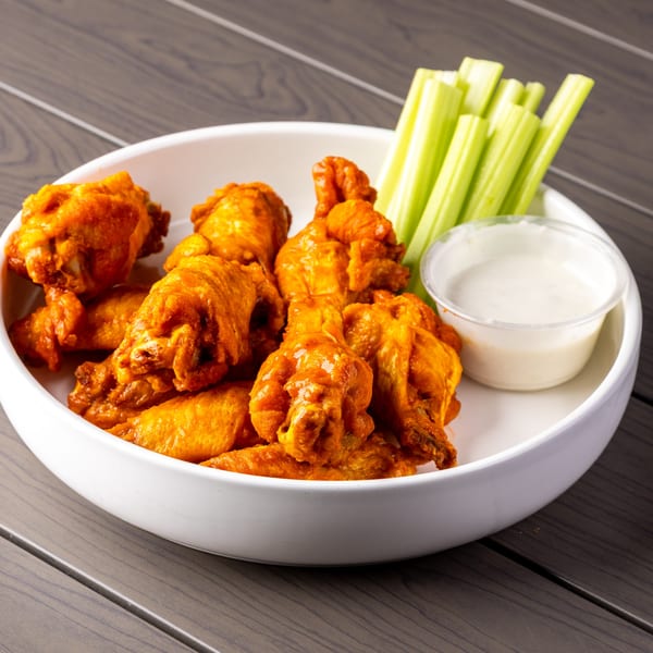 A white bowl filled with Annie's hot wings, celery sticks, and a side of ranch dressing.