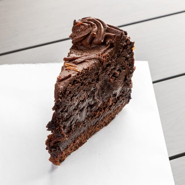 A rich slice of chocolate cake with chocolate frosting and shavings on a white napkin.