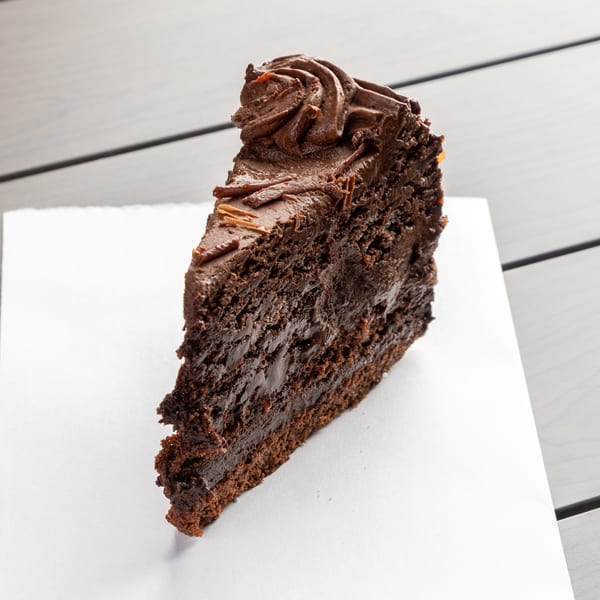 A rich slice of chocolate cake with chocolate frosting and shavings on a white napkin.