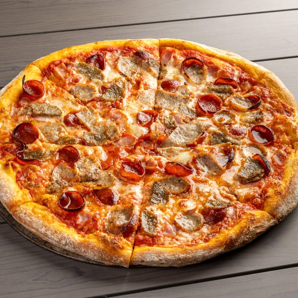 A whole Annie's Pizza with pepperoni, sausage, and bacon on a dark wooden table.