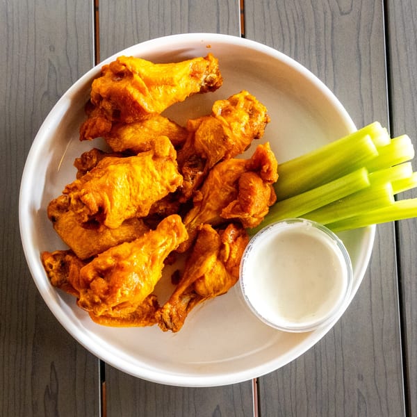 A white plate of Annie's Pizza Subs & Wings' buffalo wings, celery sticks, and ranch dressing.