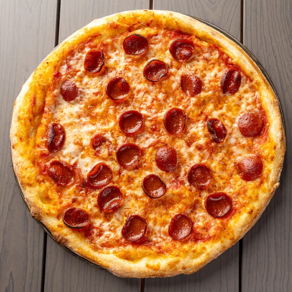 A whole pepperoni pizza with melted cheese and a golden crust sits on a dark wooden table.