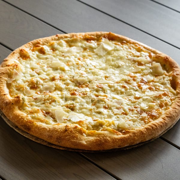 Annie's Pizza Subs & Wings white pizza with a golden crust and shaved cheese on a dark table.