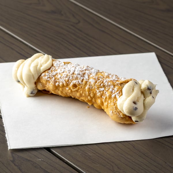 A cannoli from Annie's Pizza Subs & Wings, filled with cream and sprinkled with powdered sugar.