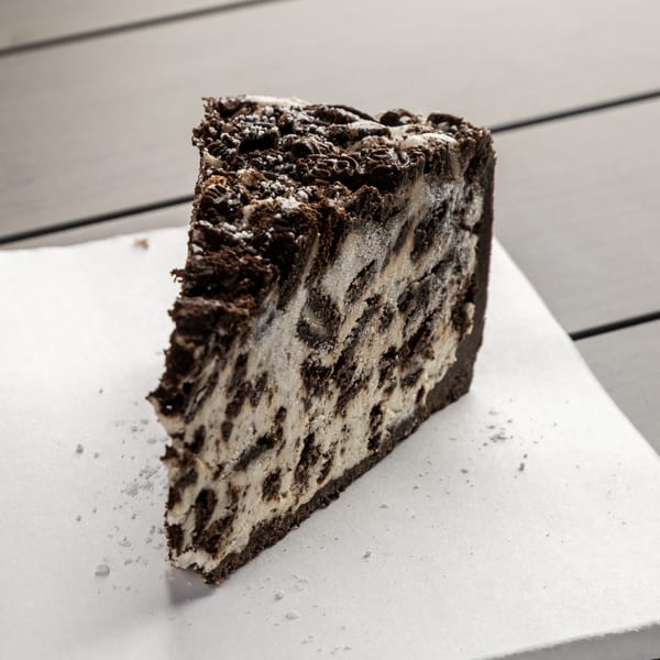 A slice of cookies and cream cheesecake with a chocolate crust, dusted with powdered sugar.